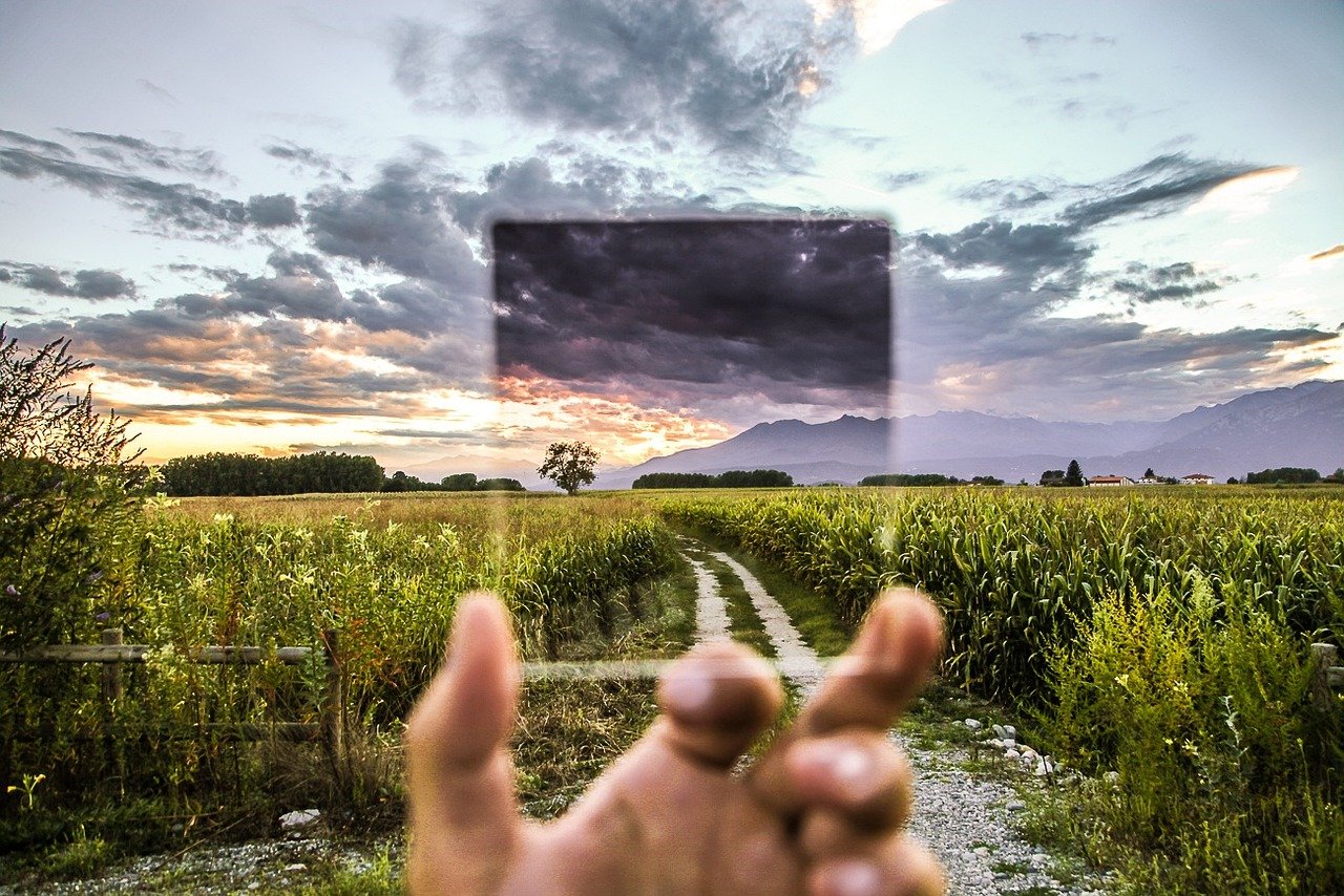 A hand reaching toward a translucent screen above an open field at sunset